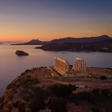 Sunset over the a temple's rising columns with water and mountains in the background