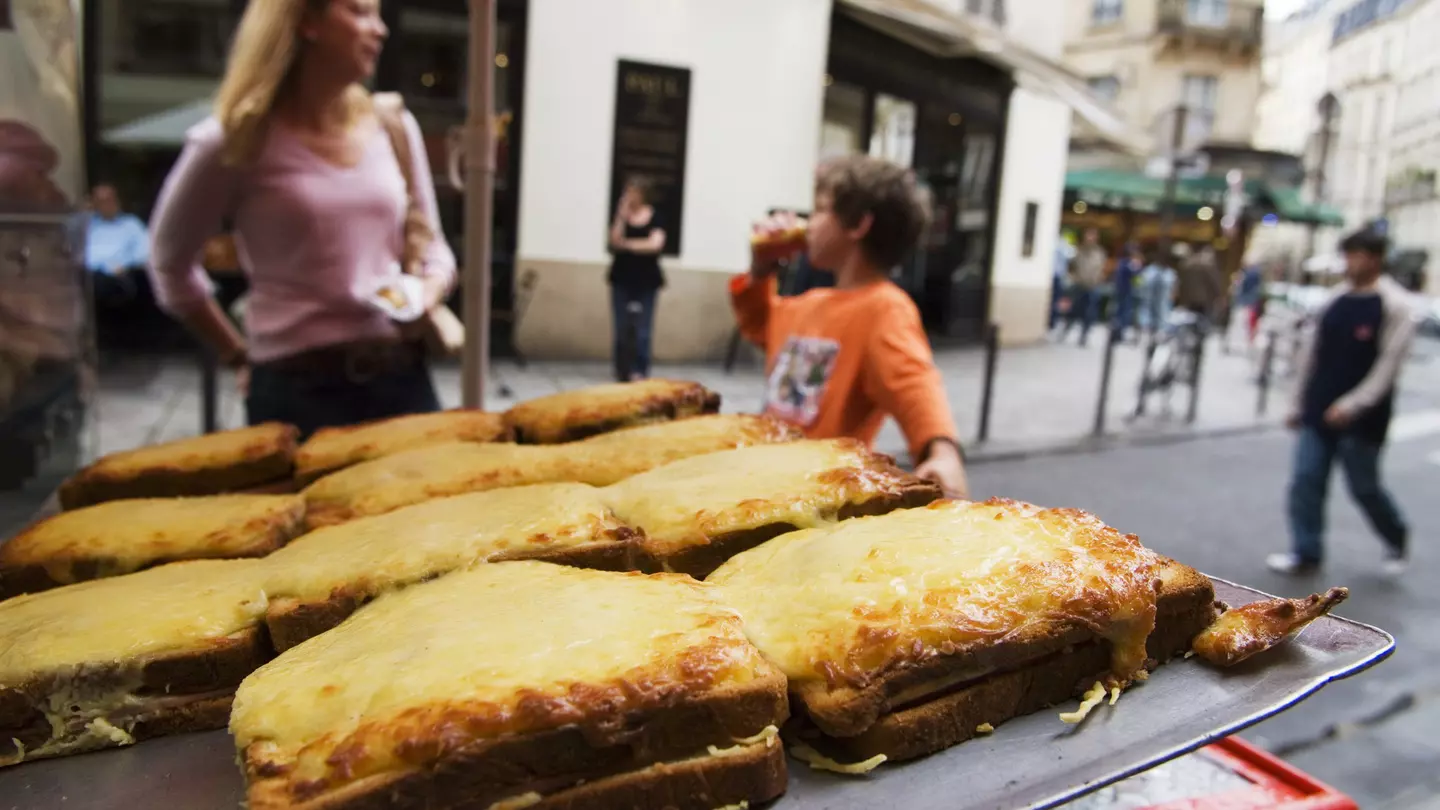 A display of croques (toasted cheese sandwiches) on sale on the street in Place St-Germain des Pres area with people in soft focus in the background.