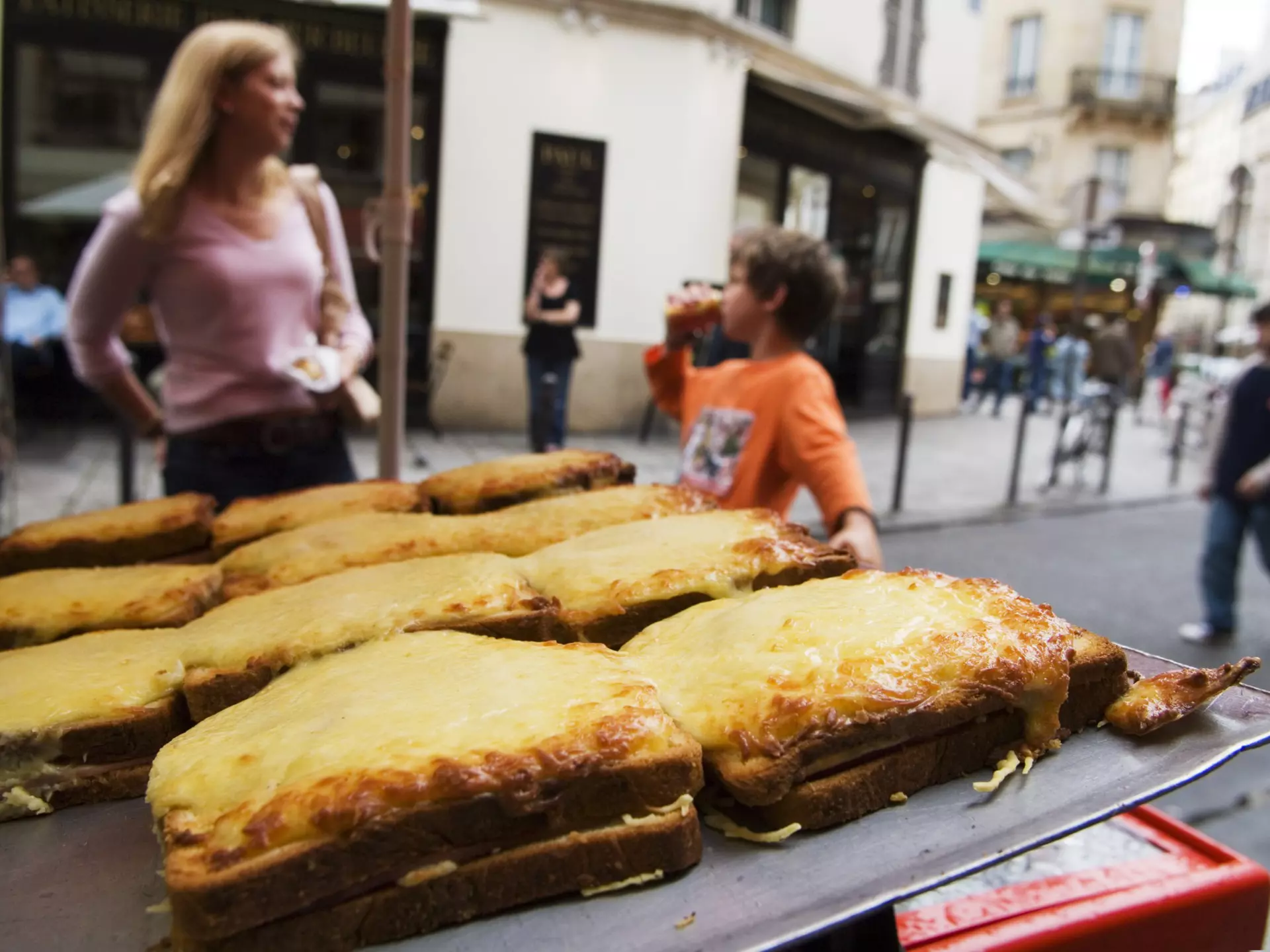 A display of croques (toasted cheese sandwiches) on sale on the street in Place St-Germain des Pres area with people in soft focus in the background.