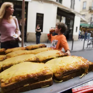 A display of croques (toasted cheese sandwiches) on sale on the street in Place St-Germain des Pres area with people in soft focus in the background.