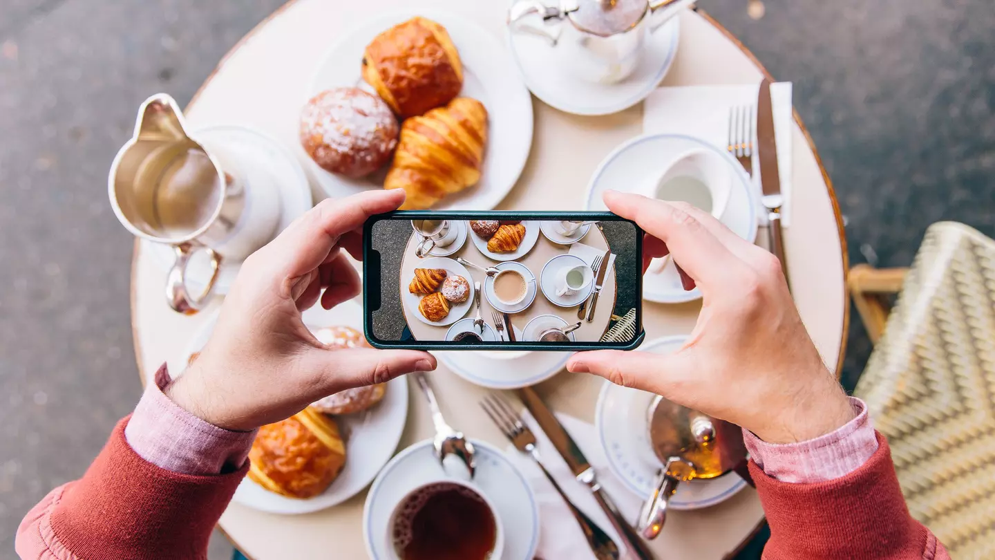 A man points to a plate of food while standing in front of a wooden door painted in the Puerto Rican flag.