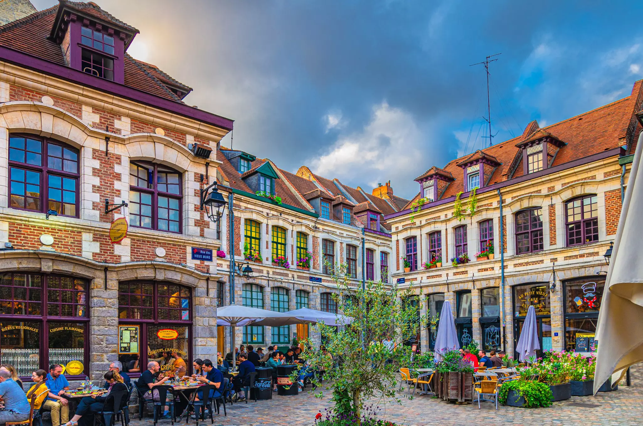 A small city square lined with historic buildings. Restaurants, bars and cafes serve diners at outside tables.