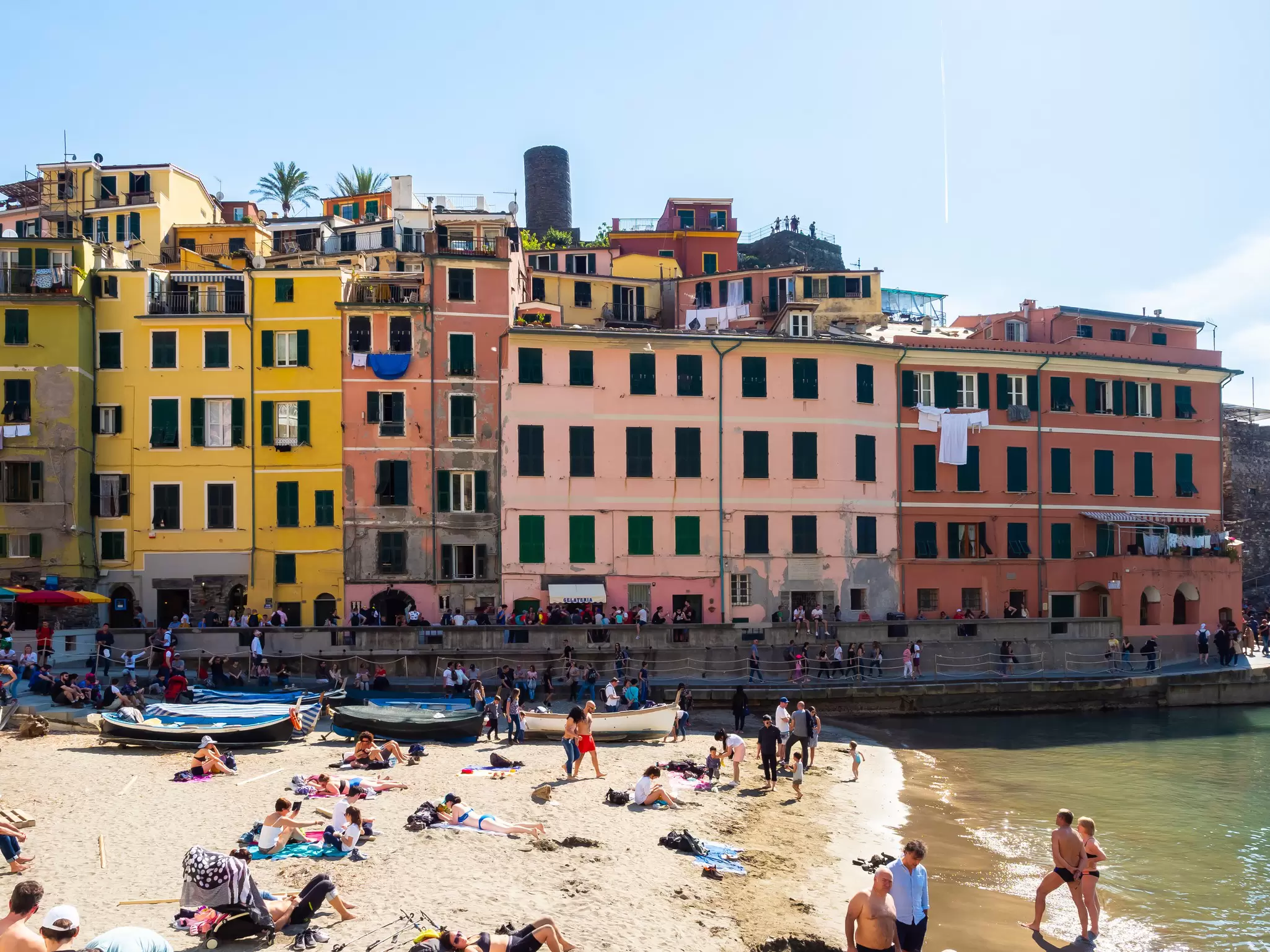 Sunbathers on a beach at a small harbor surrounded by colorful buildings