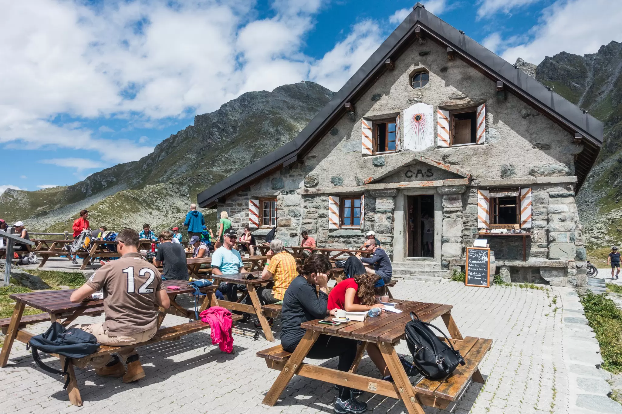 hikers sit at tables outside Cabane Mont Fort on a sunny day