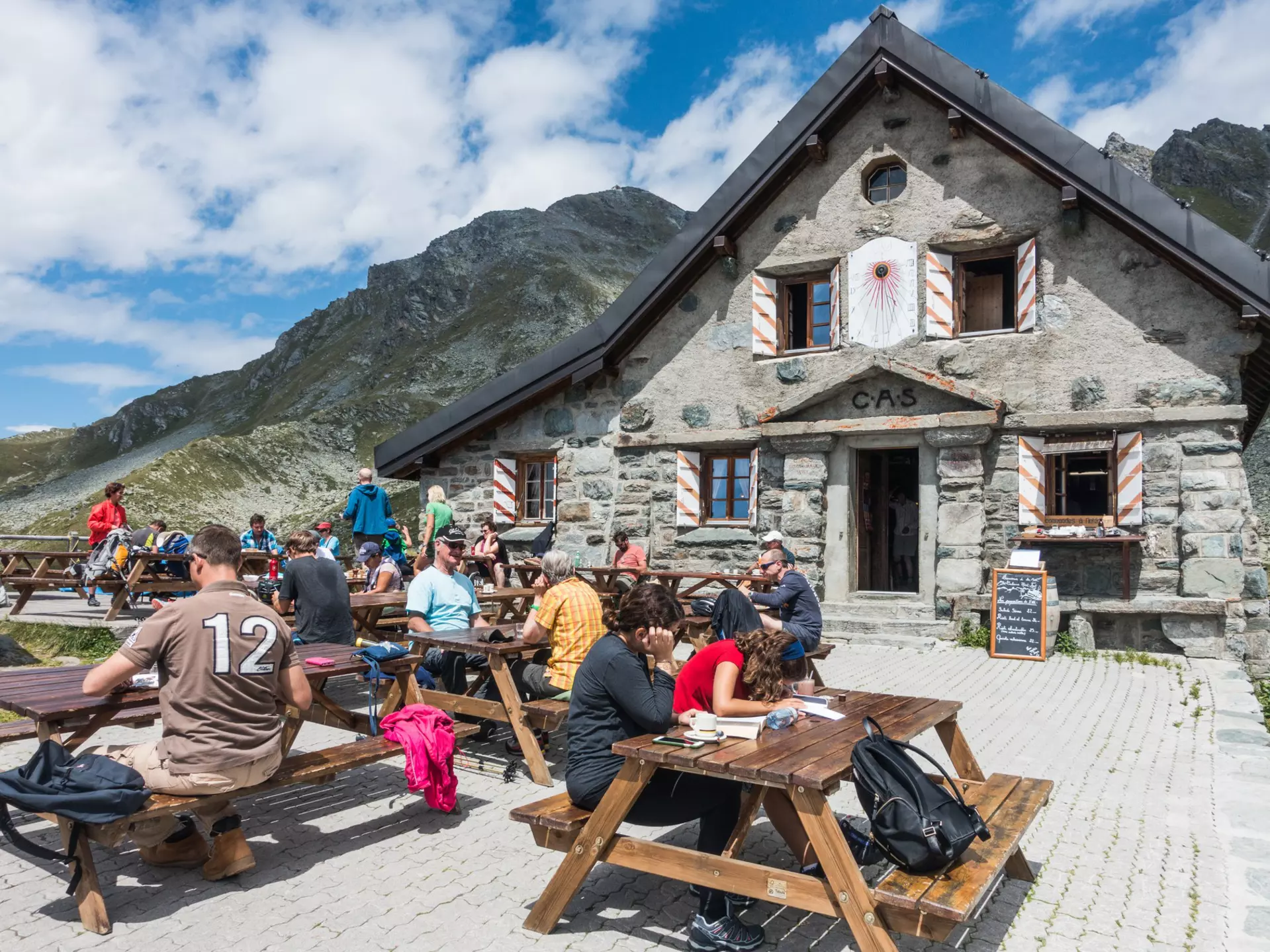 hikers sit at tables outside Cabane Mont Fort on a sunny day