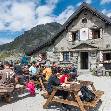 hikers sit at tables outside Cabane Mont Fort on a sunny day