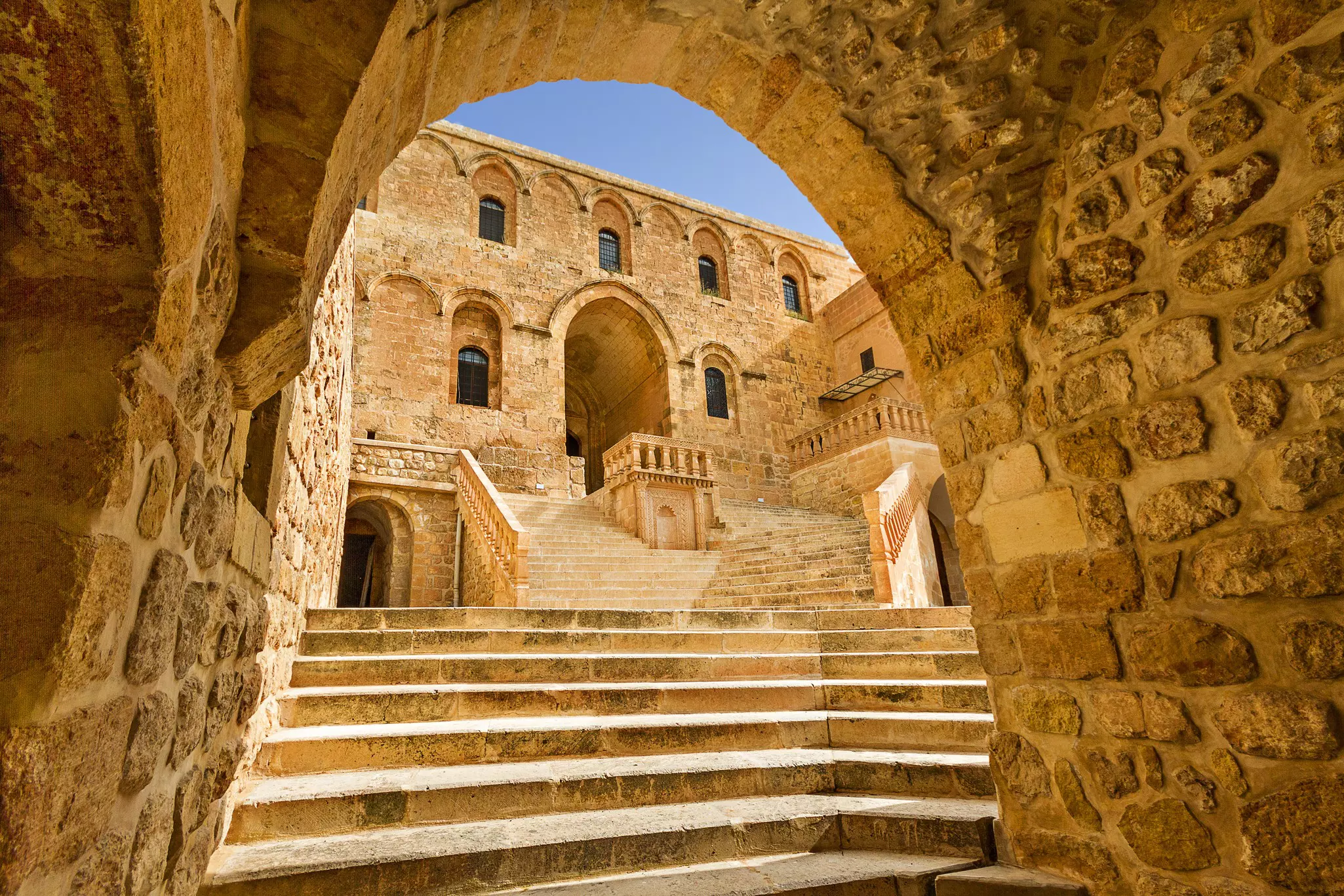 The bright yellow stone monastery seen through a stone arch. 