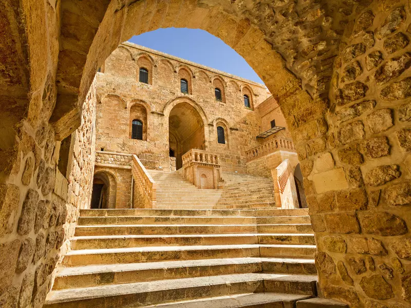 The bright yellow stone monastery seen through a stone arch. 