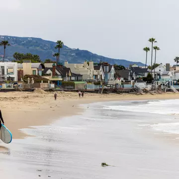 A surfer walking along the beach in Malibu. 