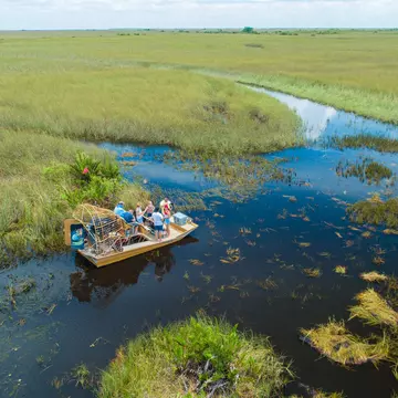An aerial view of people on an airboat stopped in a wetland of grass and water inlets.