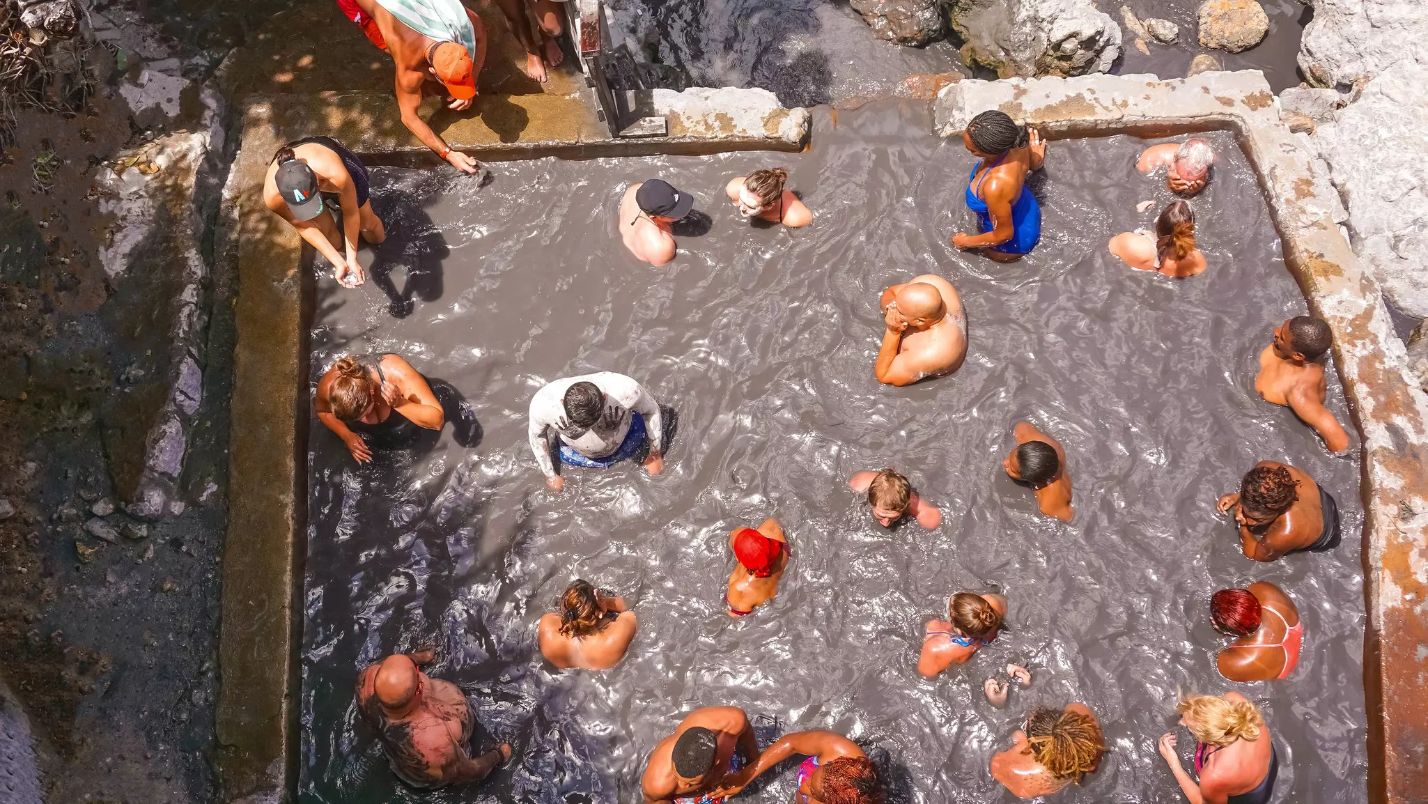 An overhead view of people soaking in a both filled with volcanically heated mud and water.
