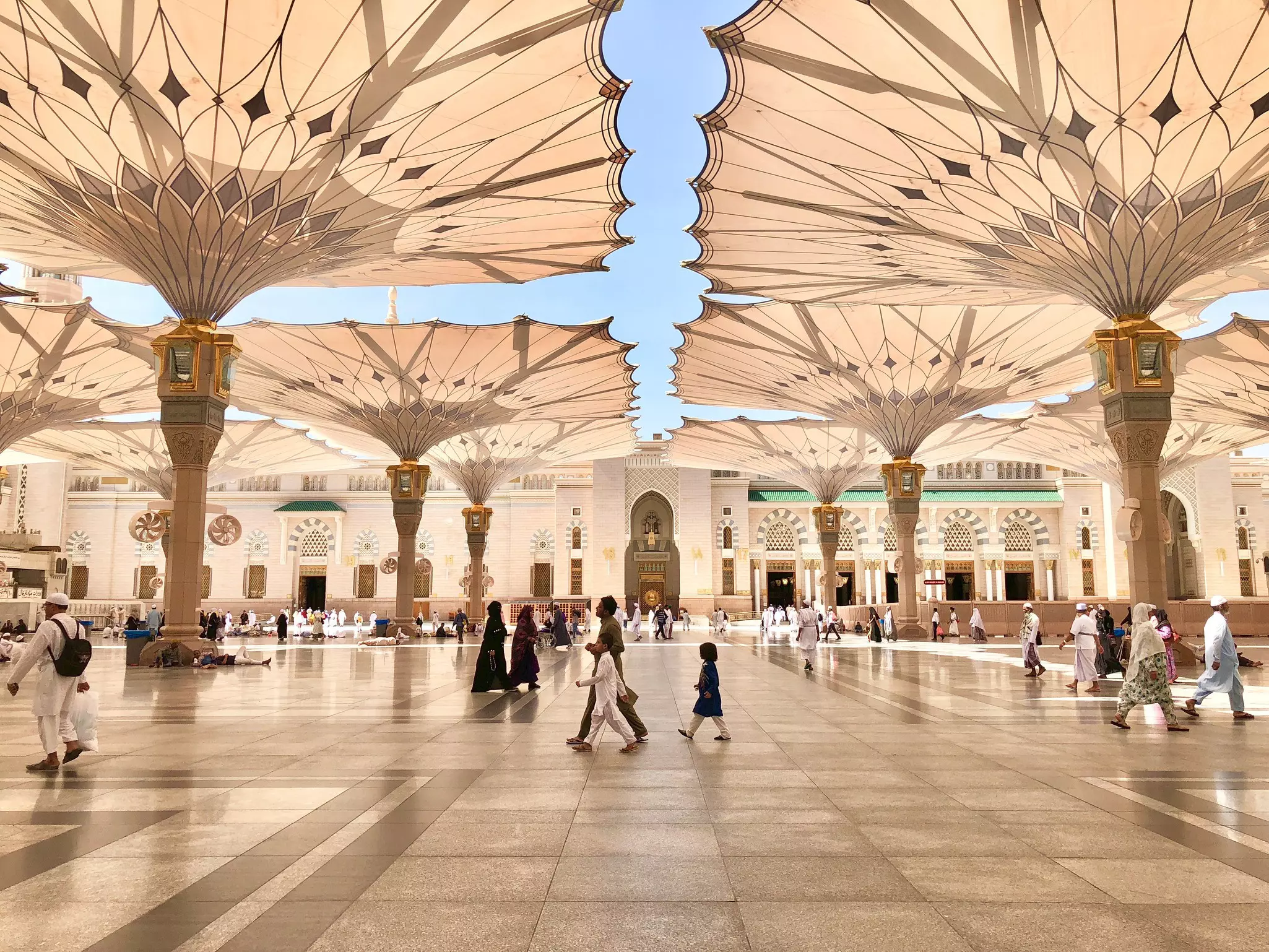 Exterior of the Nabawi Mosque in Medina (Madinah) in Saudi Arabia, with visitors walking by under sunshades.