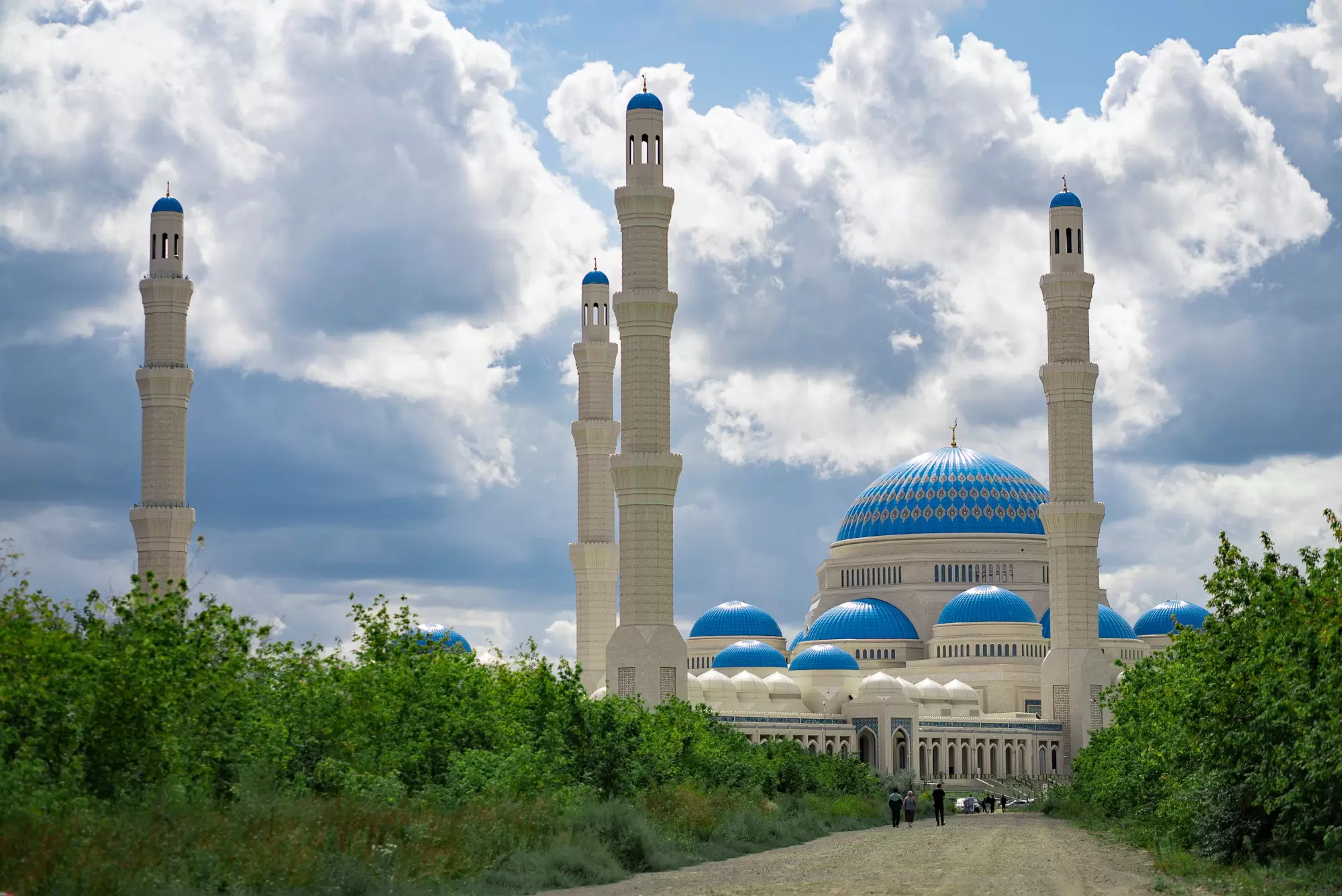 People on a road in front of the tall minarets of the Astana Grand Mosque in Astana, Kazakhstan.