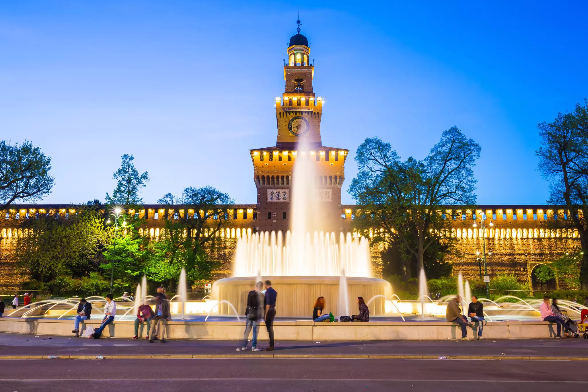 people sit around a fountain in front of Castello Sforzesco in Milan, Italy
