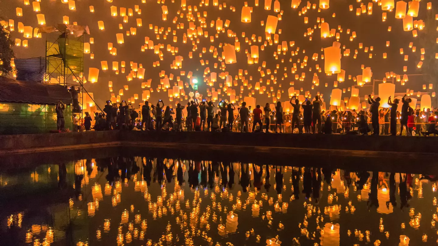 Festival goers watching Sky lanterns firework festival, Chiang Mai, with the lanterns reflecting off some water