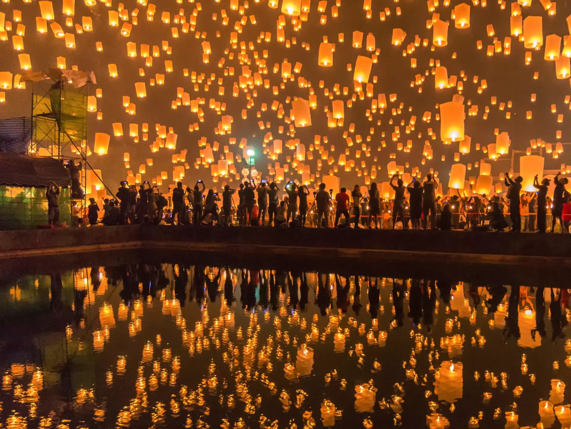 Festival goers watching Sky lanterns firework festival, Chiang Mai, with the lanterns reflecting off some water