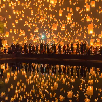 Festival goers watching Sky lanterns firework festival, Chiang Mai, with the lanterns reflecting off some water