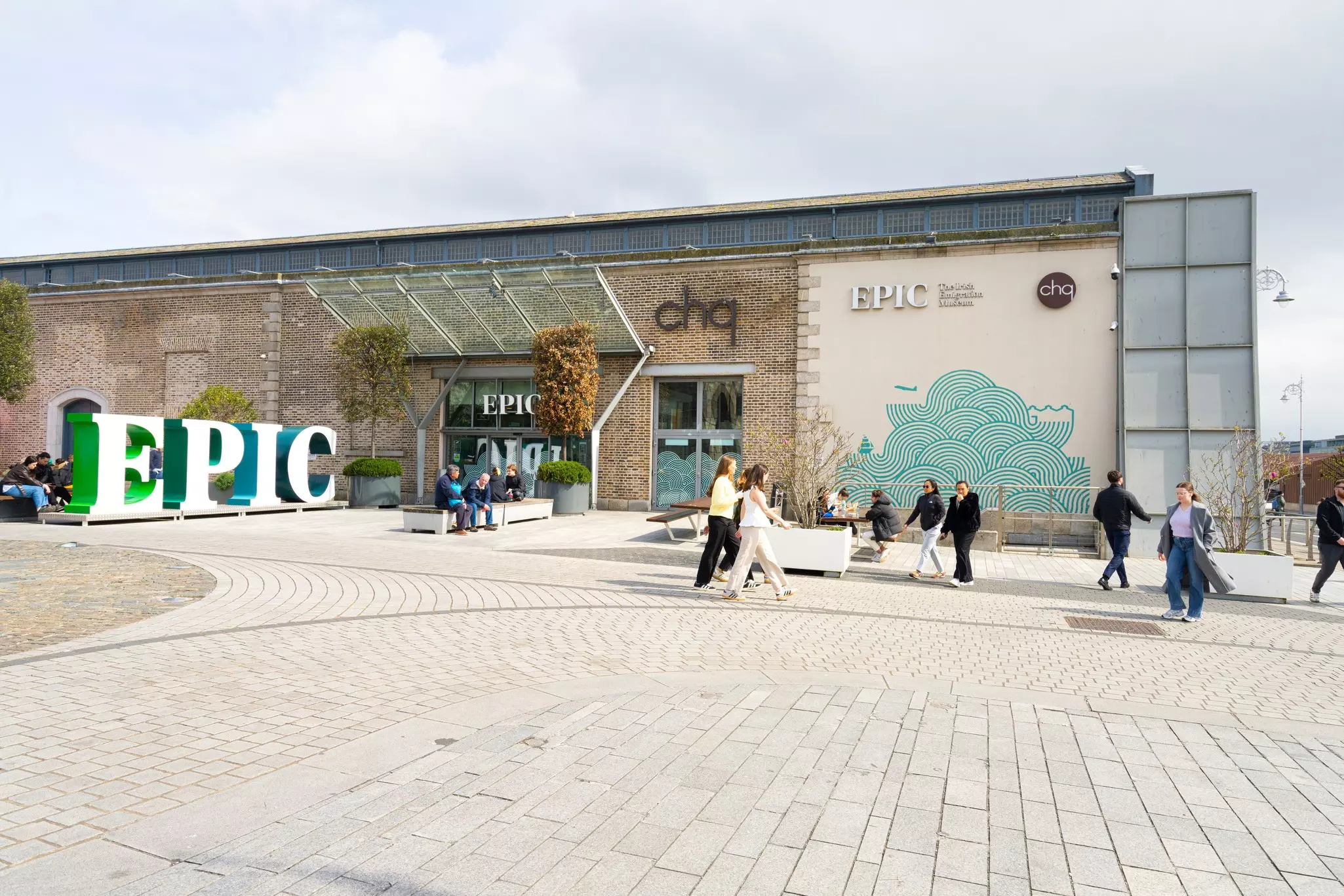 People walk through a public space outside a large museum building with signs that say "EPIC".