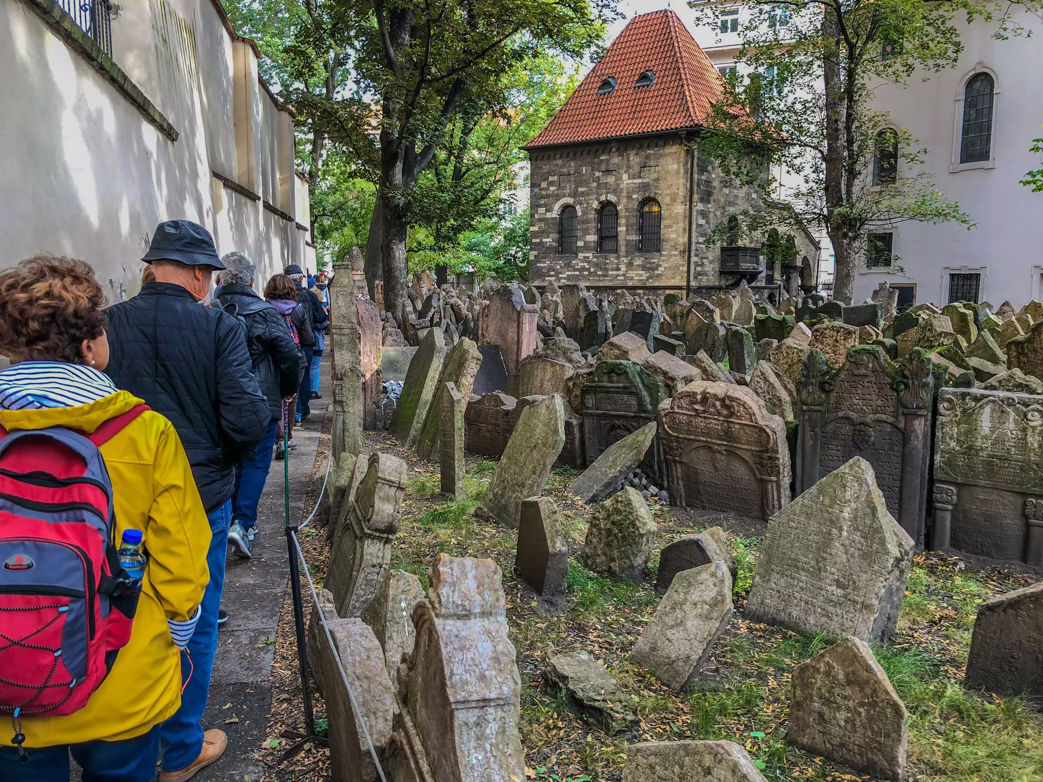 People walk in a line past a cemetery crowded with headstones.