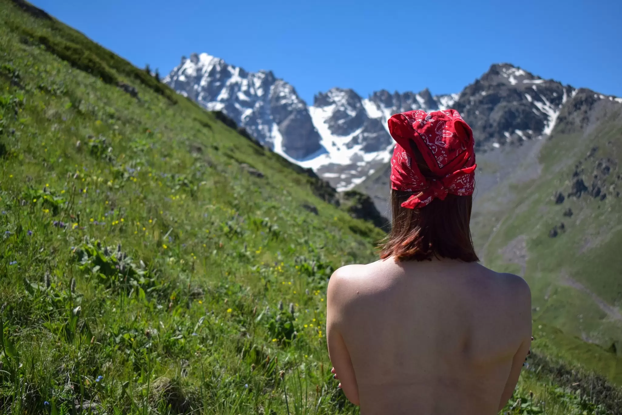 Back topless view of white woman wearing red bandana in mountains of Kazakhstan.