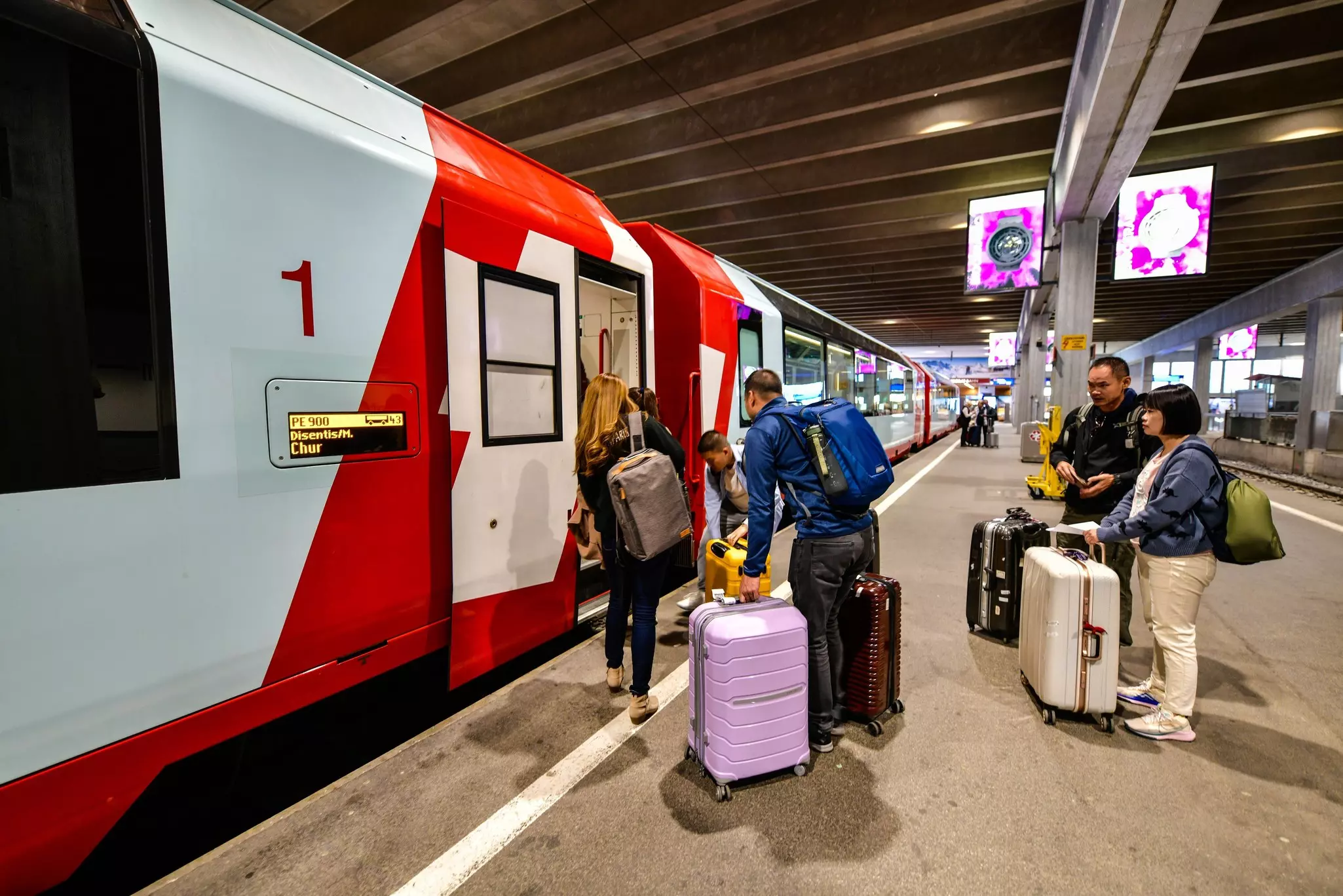 People with luggage move to board a train on the platform of a station.
