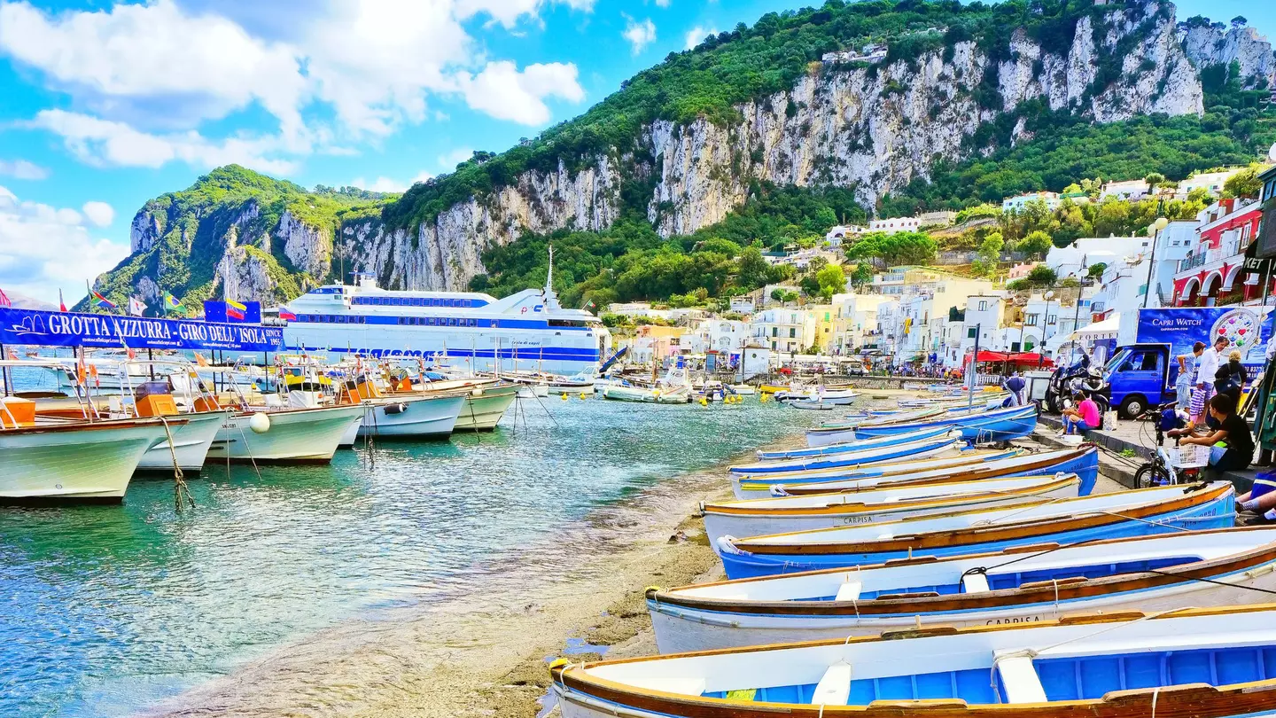 Sparkling water laps at the beach, which is lined with small white and blue boats.