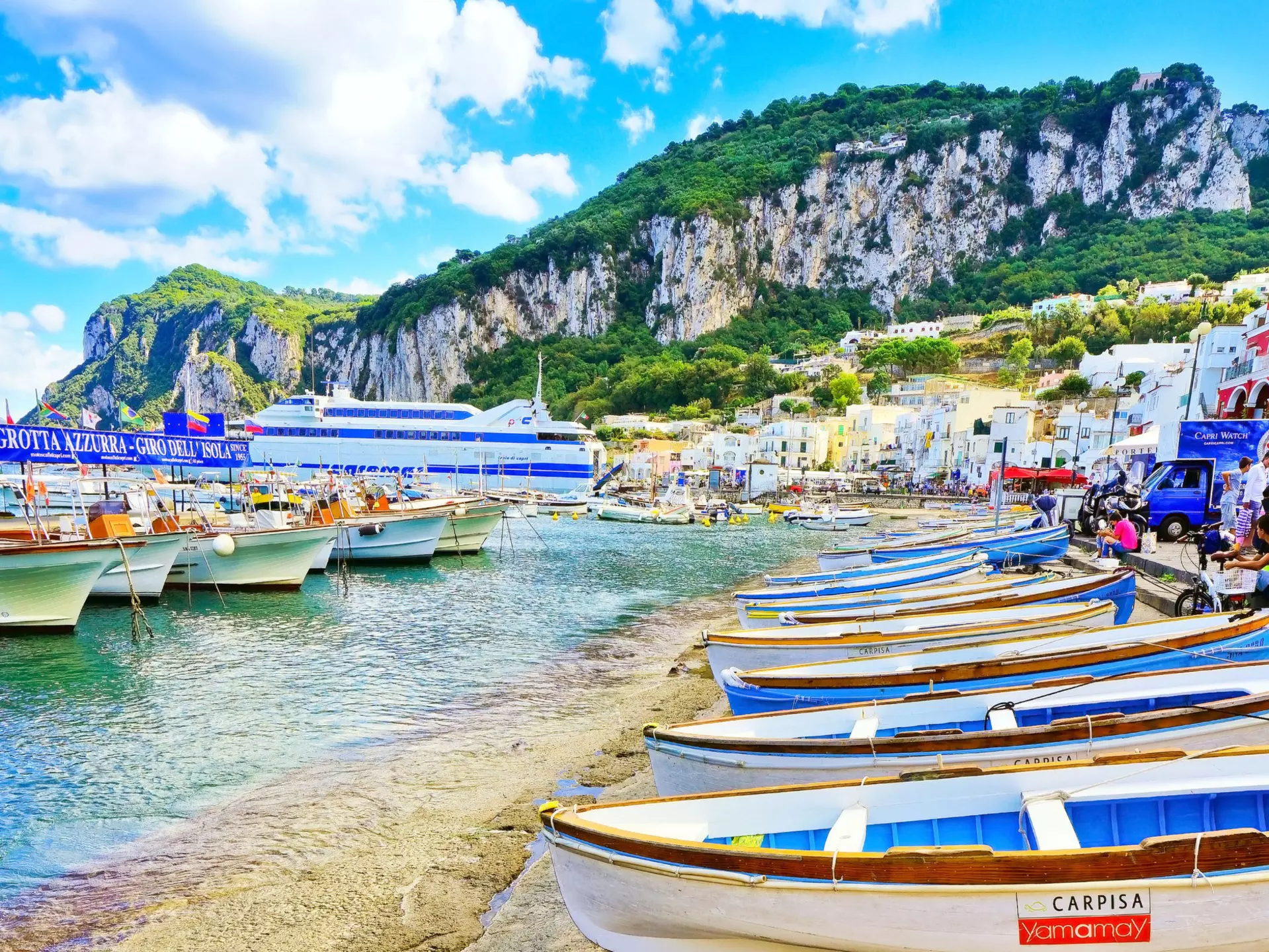 Sparkling water laps at the beach, which is lined with small white and blue boats.