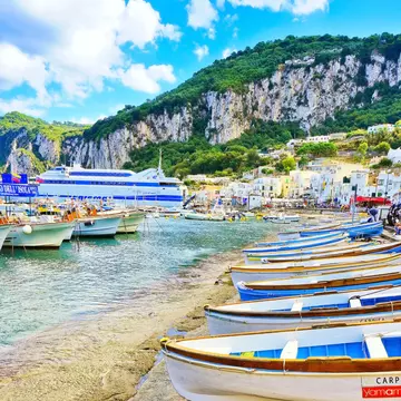 Sparkling water laps at the beach, which is lined with small white and blue boats.