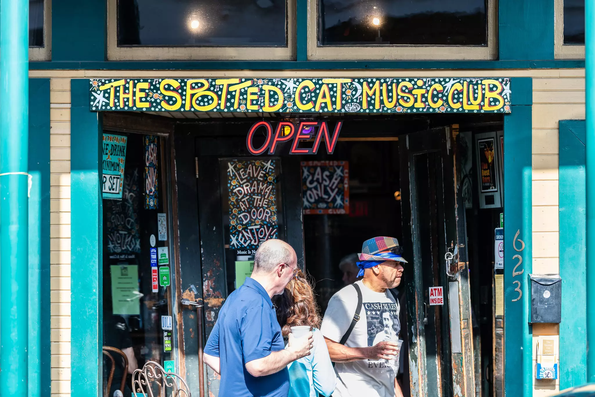 People carrying cups walk past a music club on a sunny day in New Orleans, Louisiana, USA.