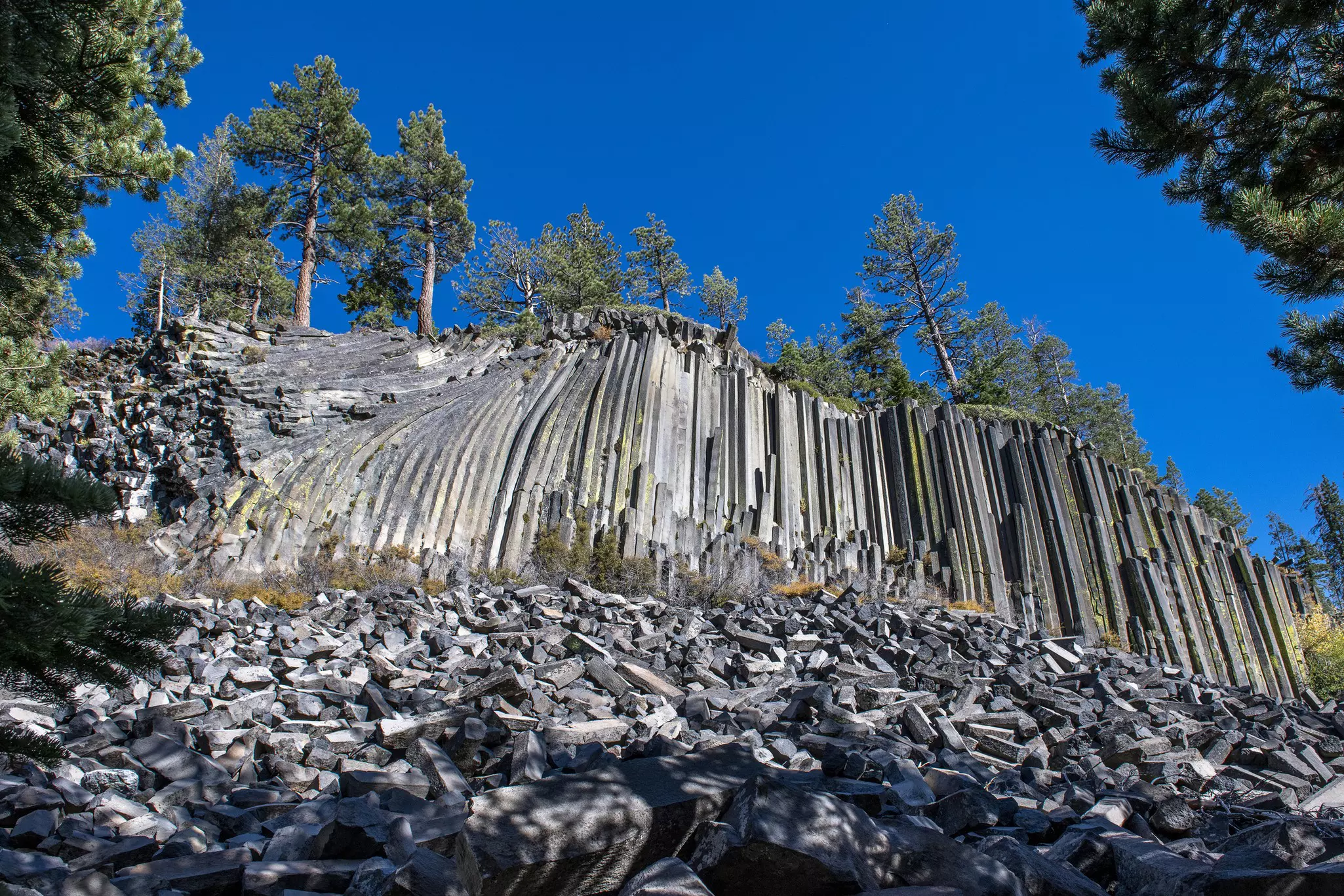 A cliff-face of basalt columns rises up from the rock-strewn ground at Devils Postpile National Monument