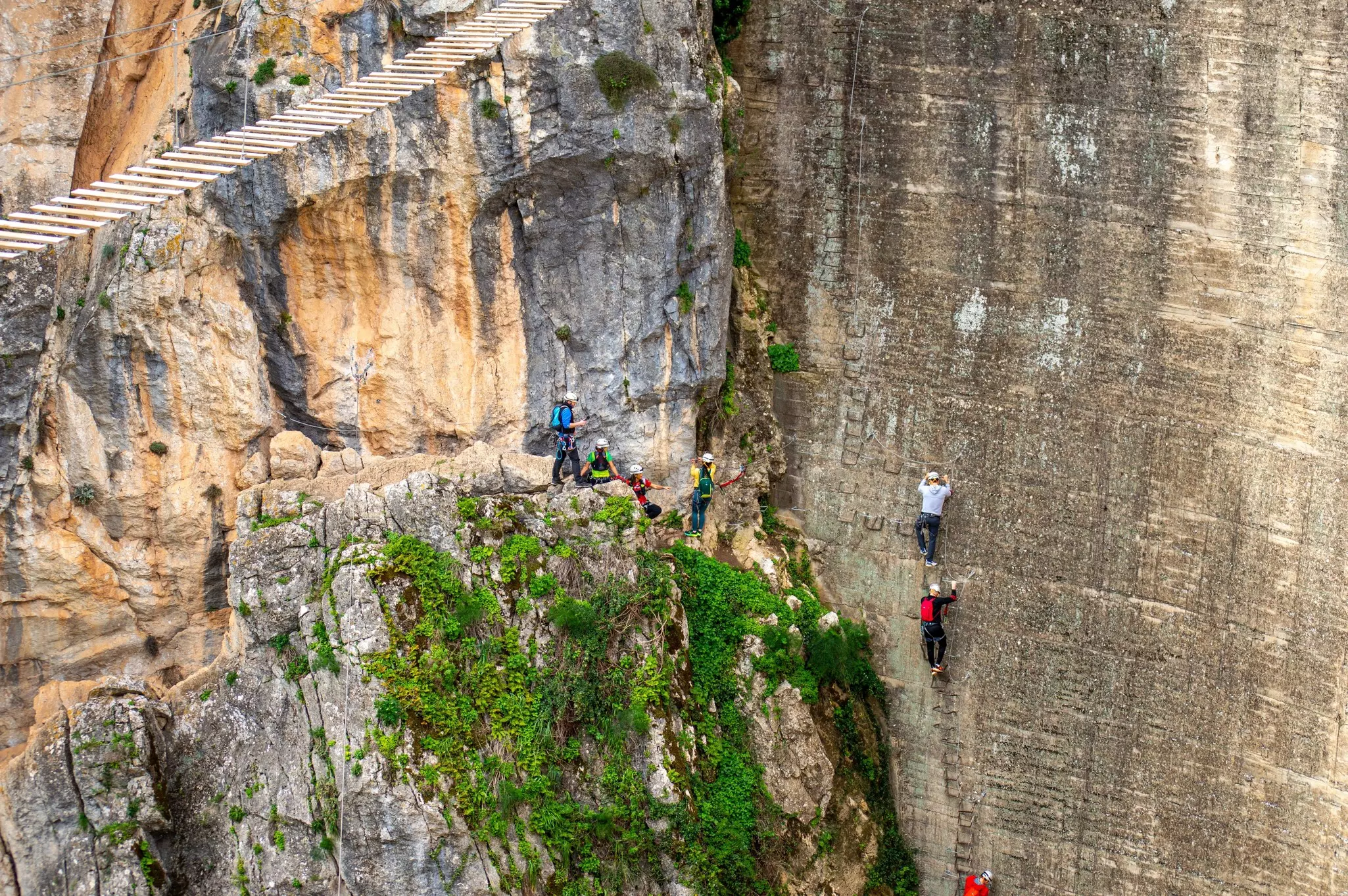 Climbers following a trail of footholds in the edge of a sheer rock face in a gorge.
