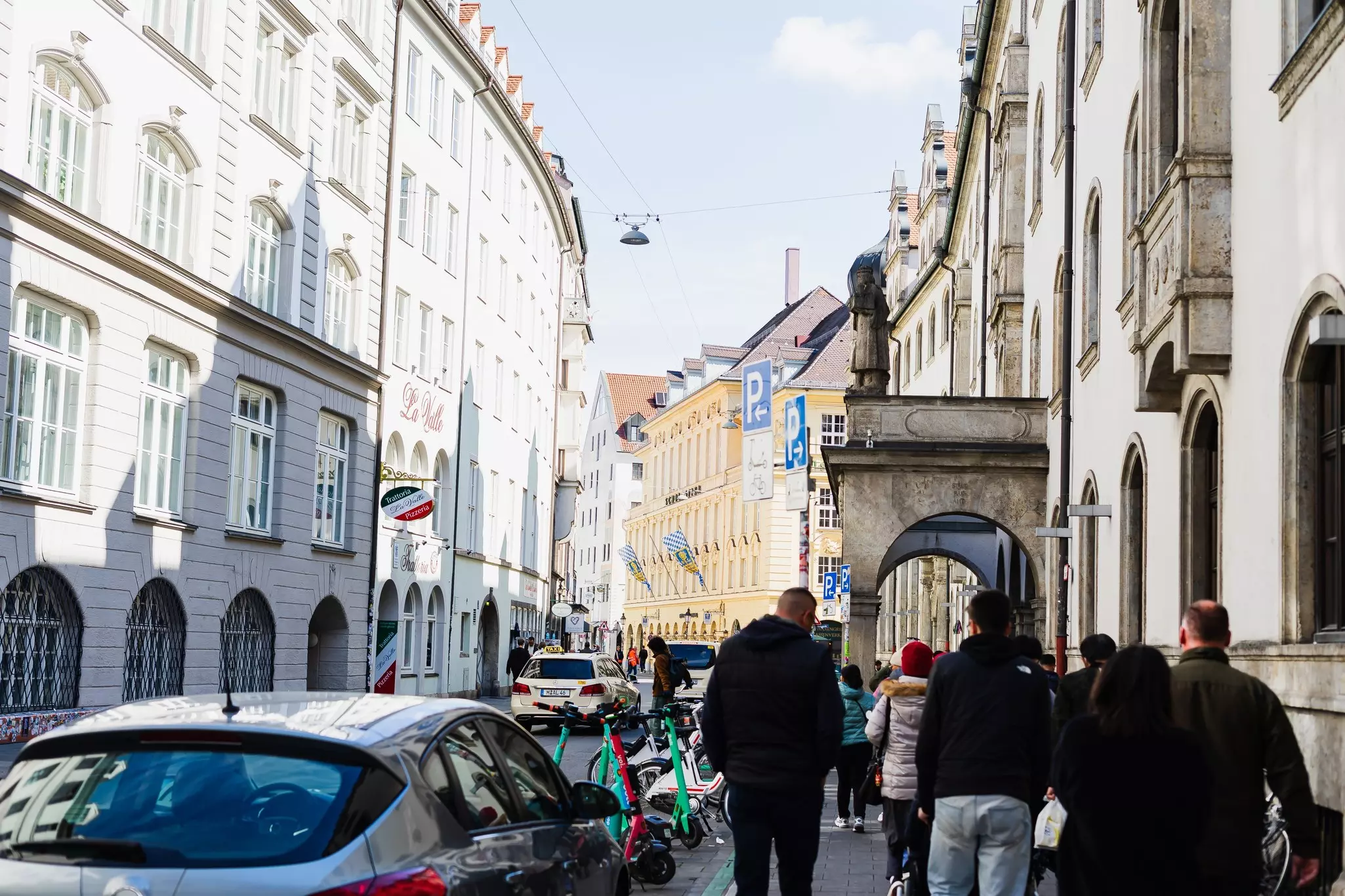 People are seen from behind walking down a narrow street in a historic district in a city.