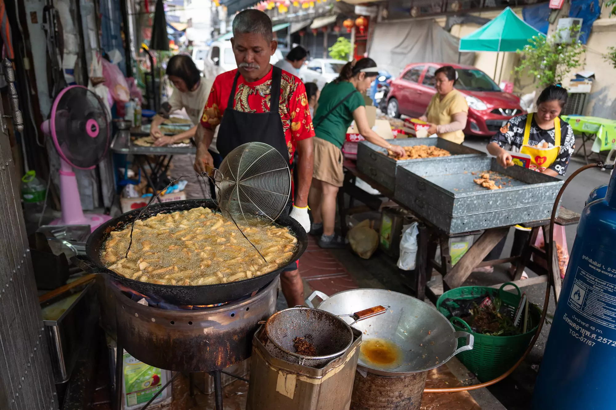 A street vendor in front of large pot of frying food.