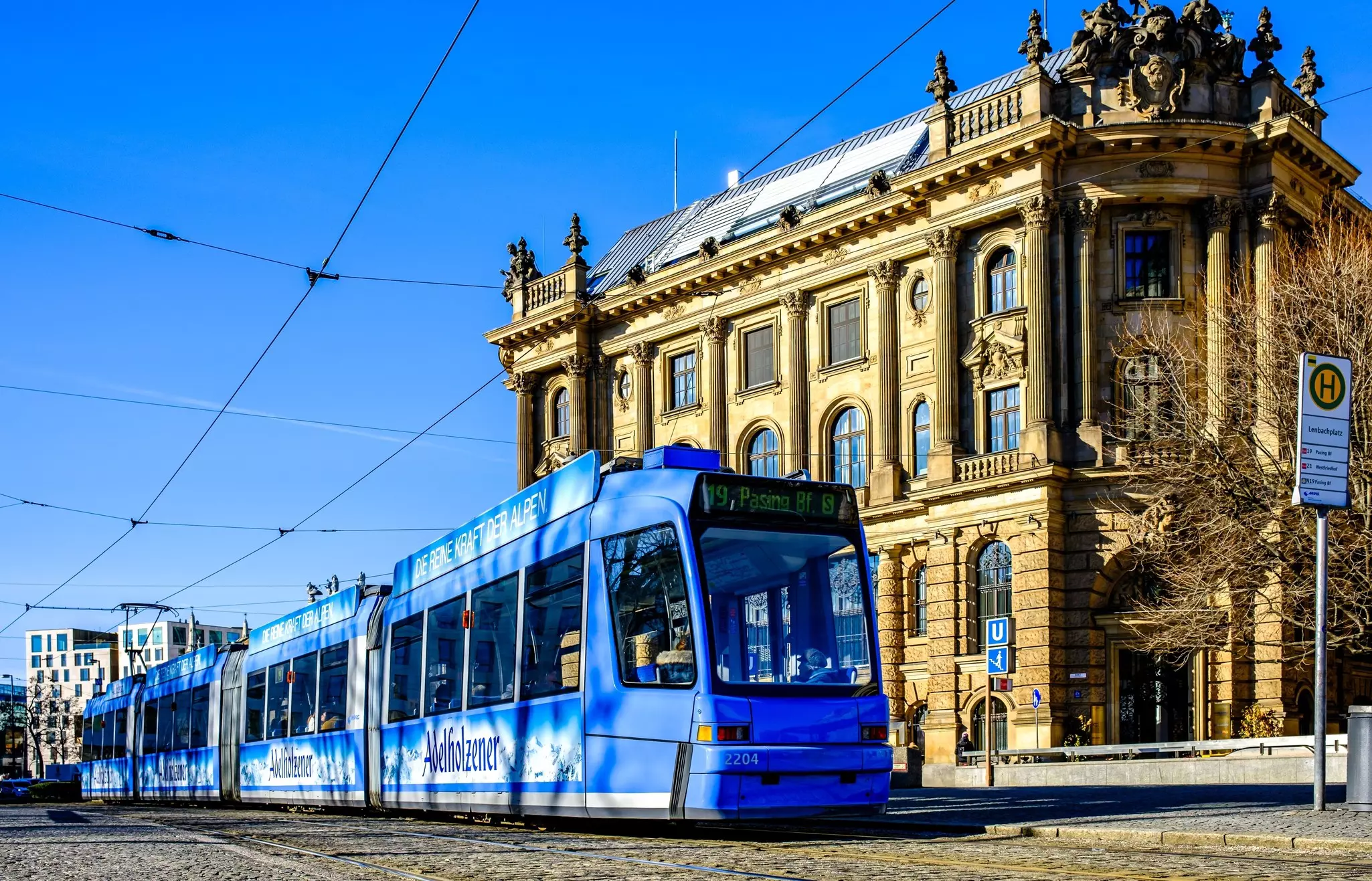 A blue tram passes by a historic building on a city street.