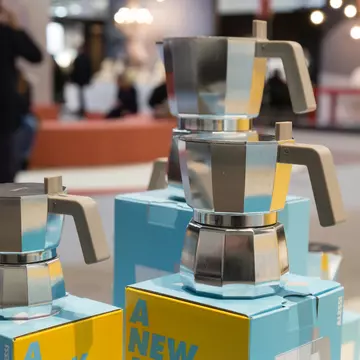A woman sits on a wooden bench in a small room and looks through a small glass window into where a prisoner would be sitting when meeting his family.