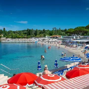 Sandy Plage de la Garoupe beach with turquoise water and red and blue parasols on Cap d'Antibes