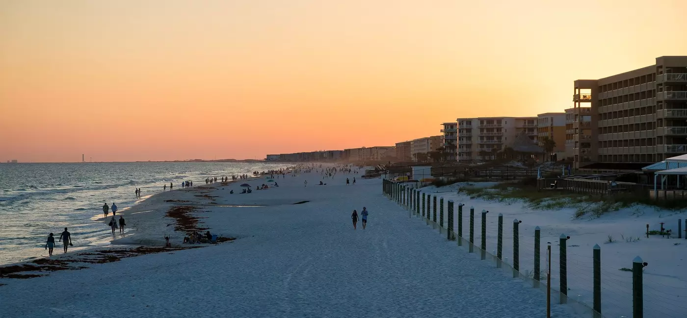 The sun sets over Okaloosa Island Pier. View from okaloosa island pier of hotels, apartments, and tourists relaxing by the sea
