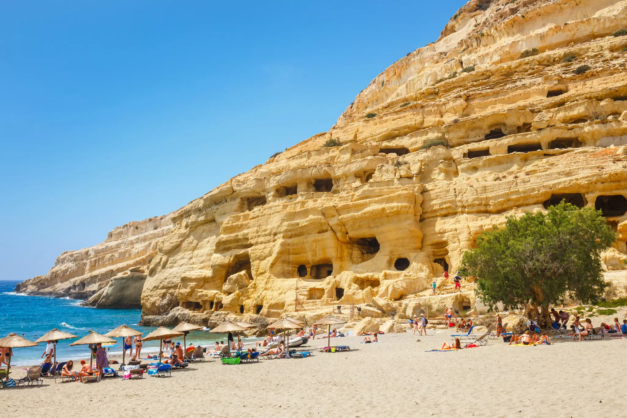 Sandy beach with sunbathers beside a hillside with rocky manmade caves