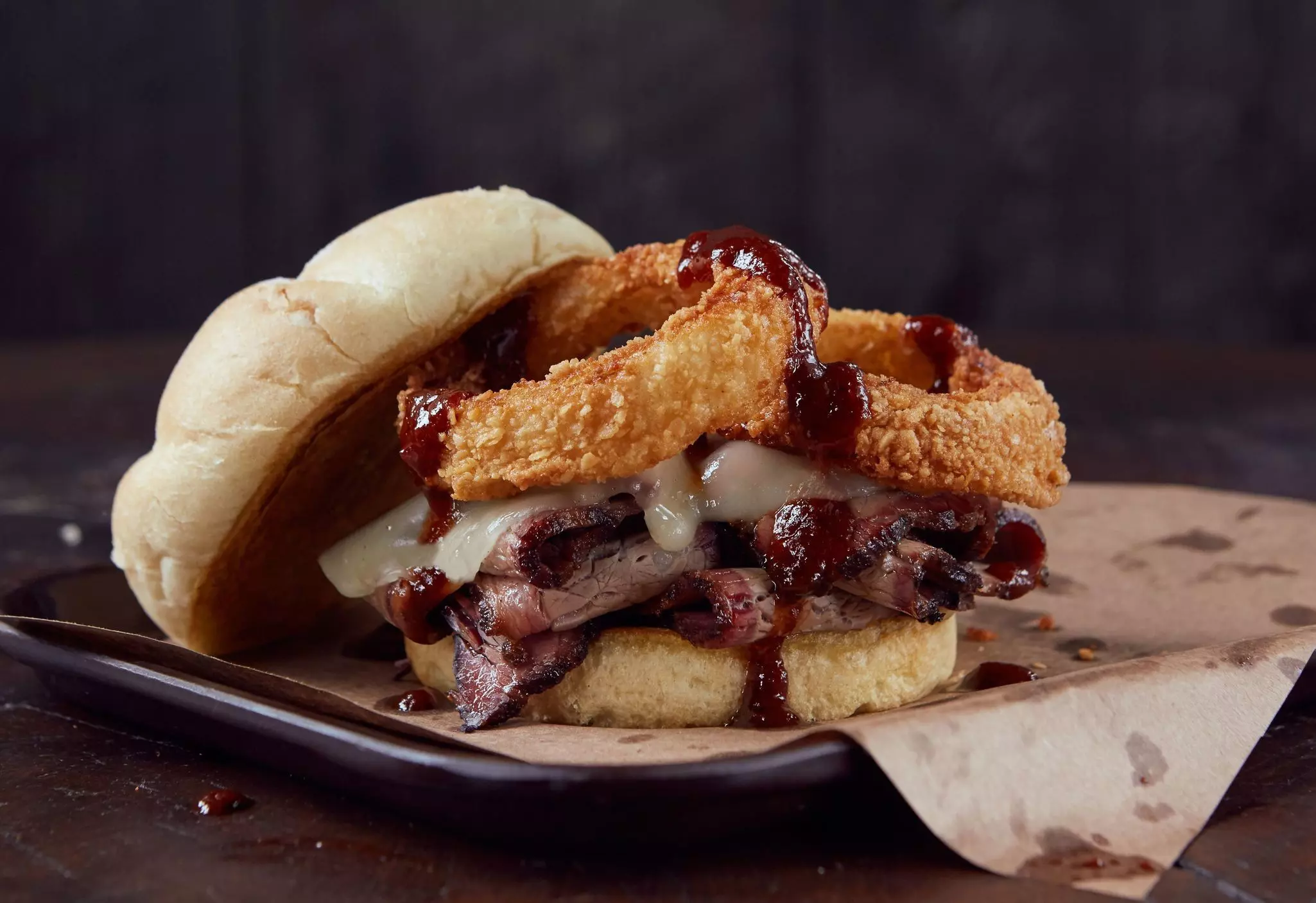 A close-up shot of a sandwich with BBQ brisket, smoked provolone cheese and onion rings on a Kaiser roll.