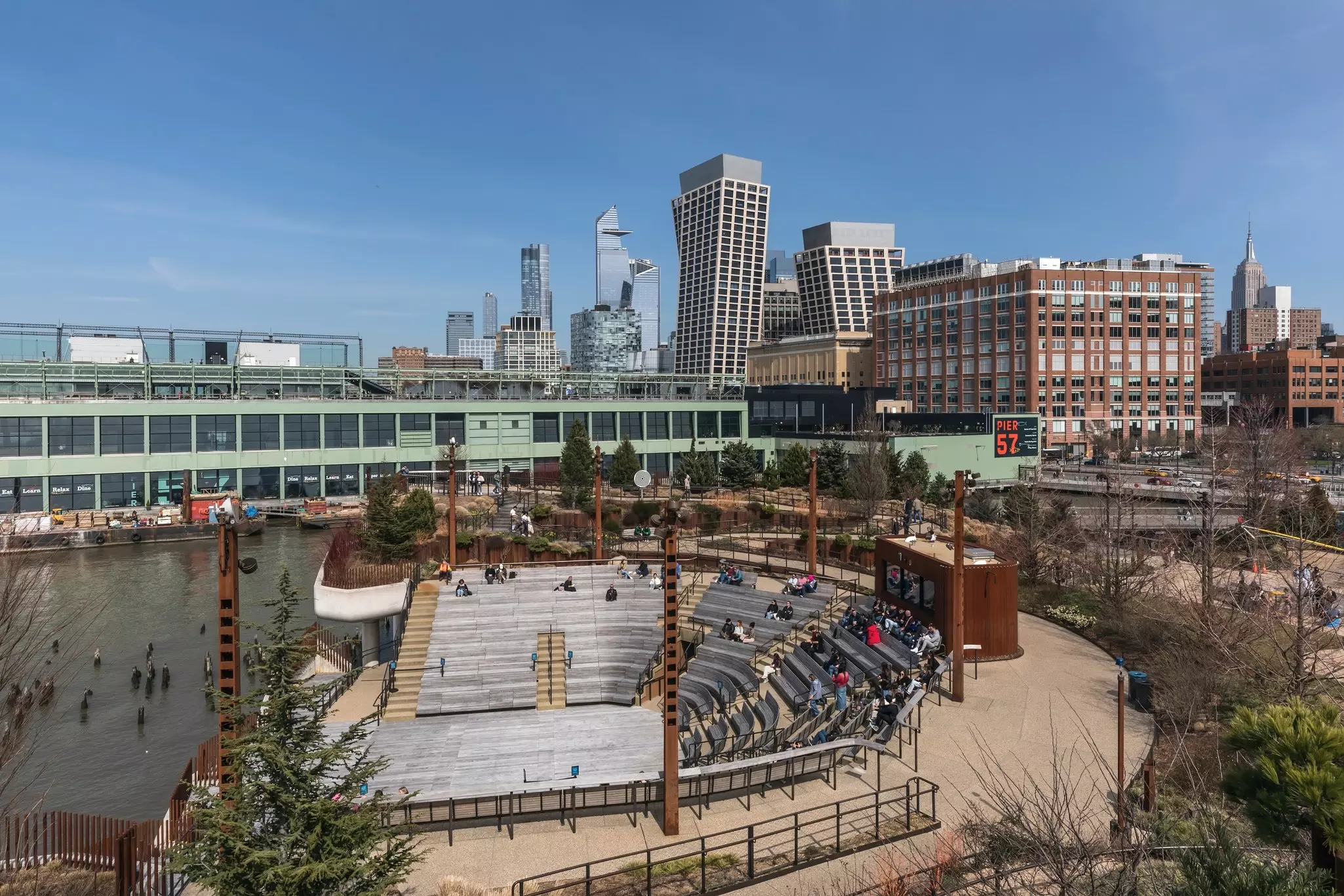 A view from above of an outdoor amphitheater at a waterside city park. Buildings of various heights are seen in the distance.