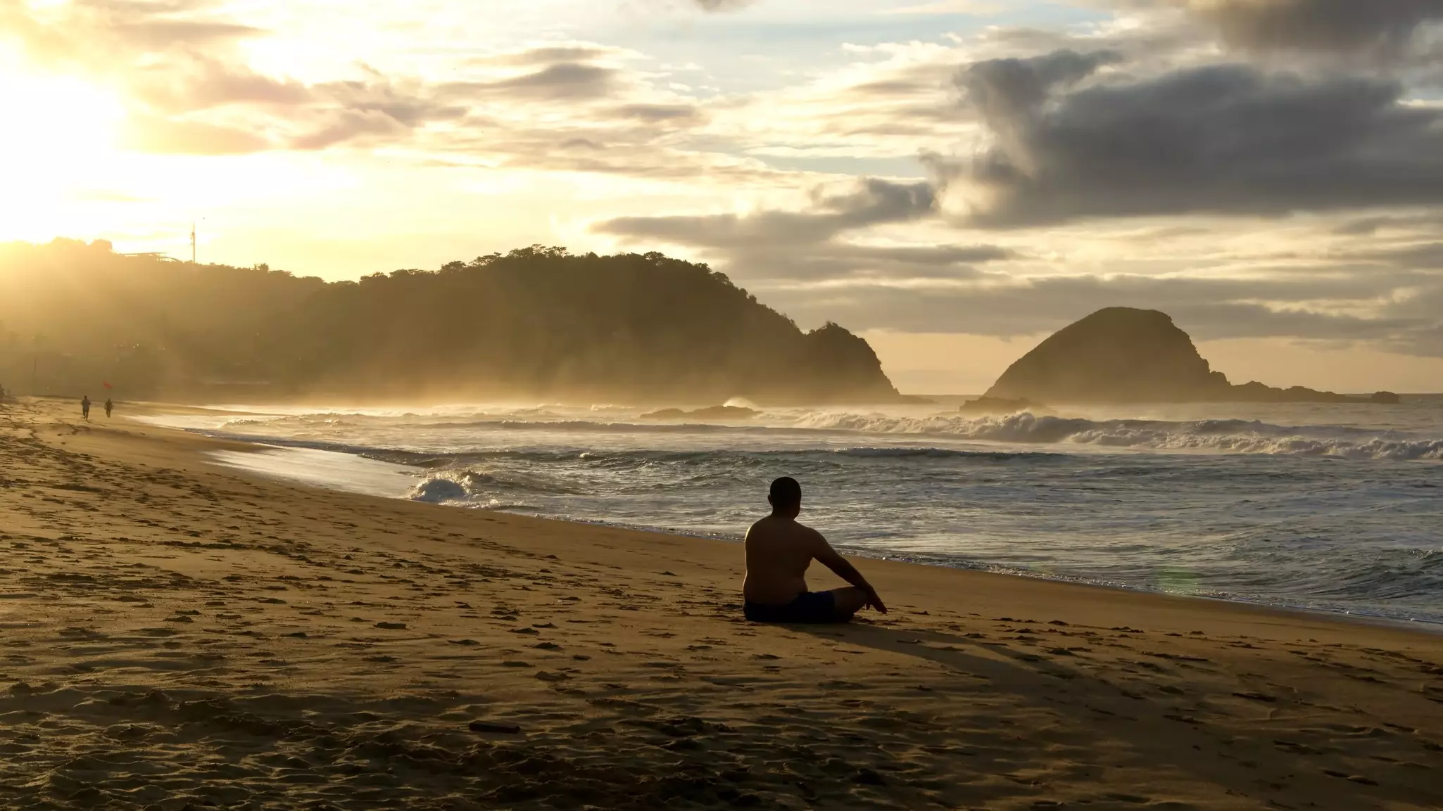 A man on a beach in silhouette at sunrise, with hills in the distance.