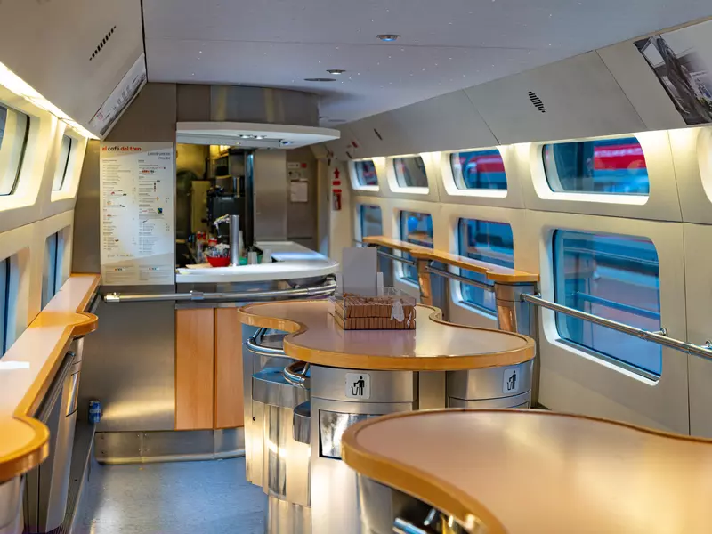 The interior of a train refreshments carriage with a counter for service and small tables for standing at.