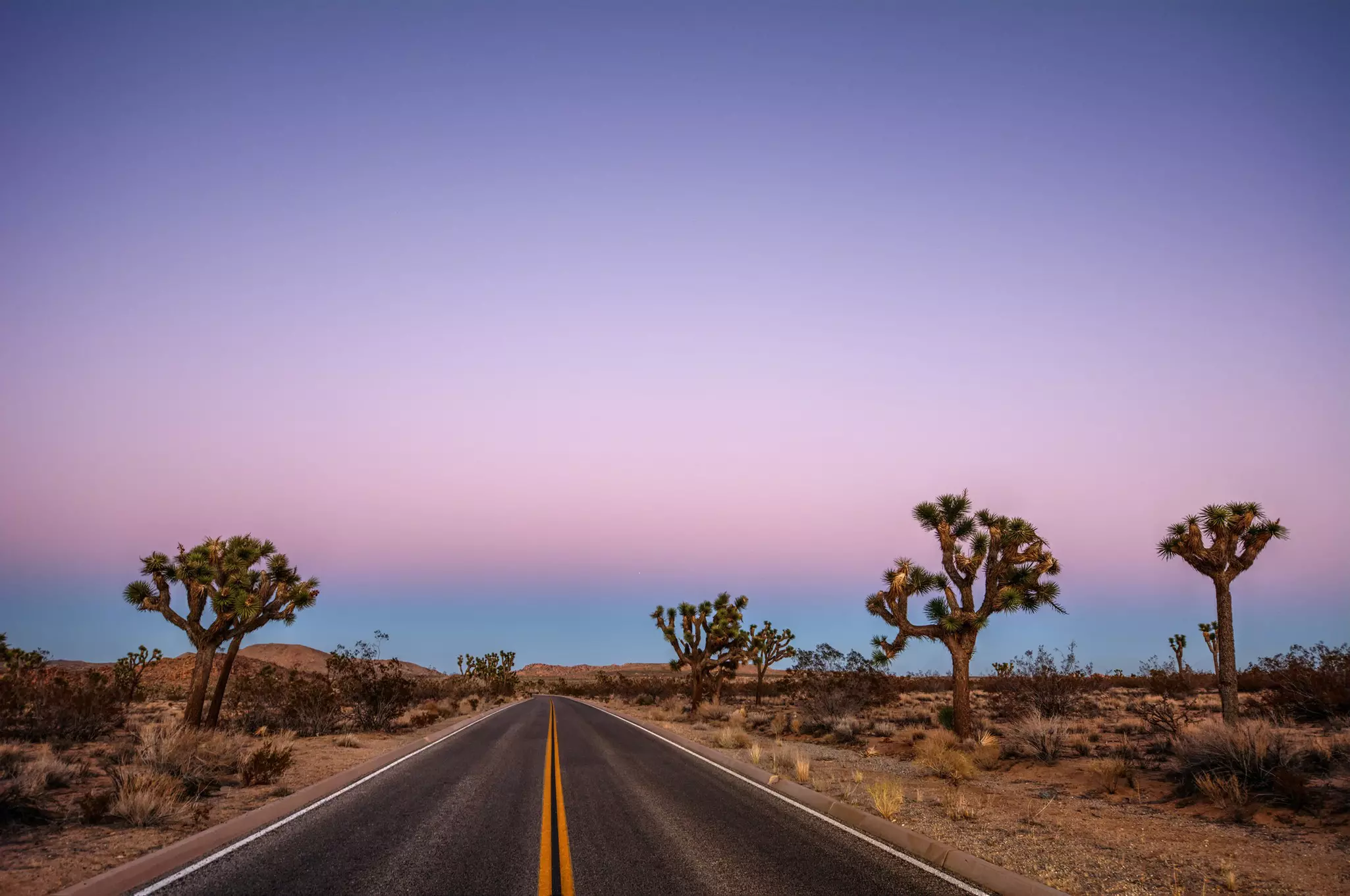 A freshly paved road at dusk running right through a desert landscape