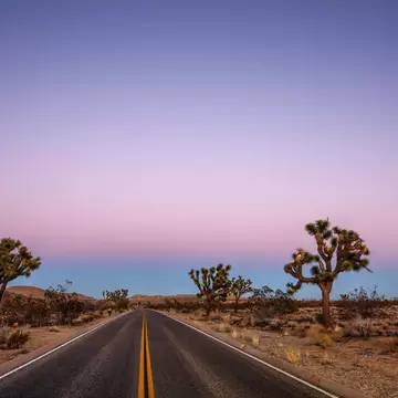 A freshly paved road at dusk running right through a desert landscape