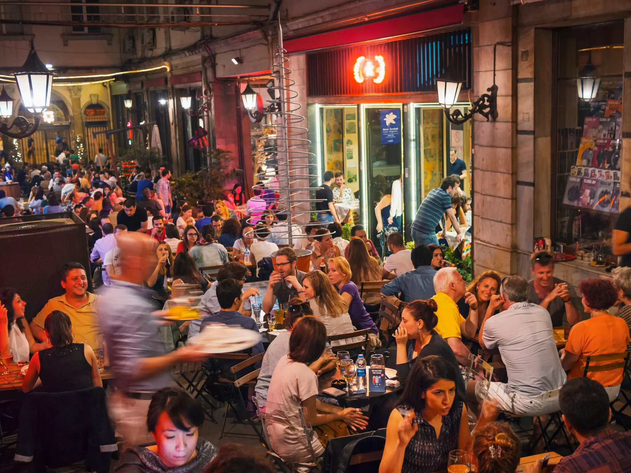 A terrace is packed with people sitting at outdoor tables at night in a city.