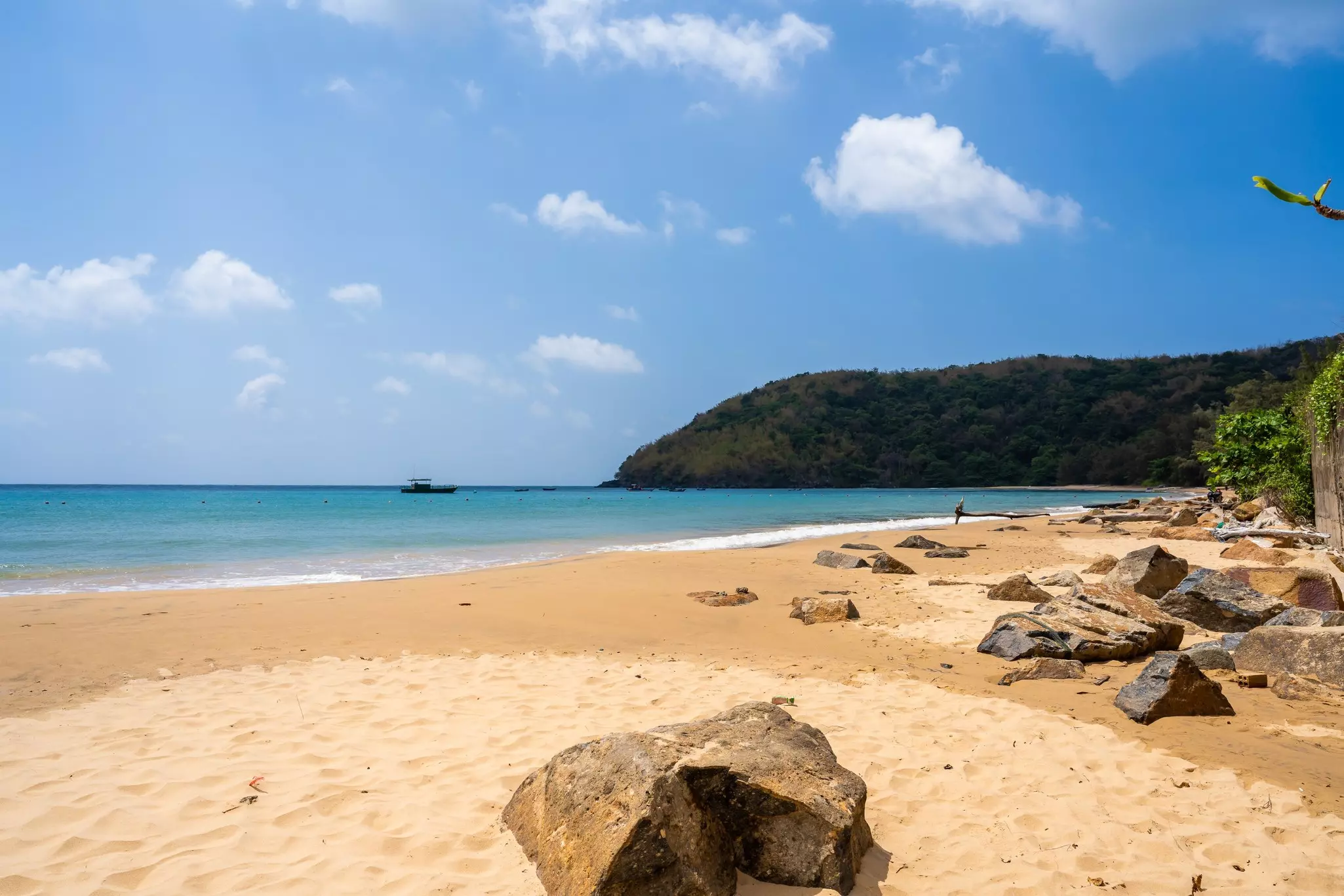 A deserted sandy beach with large boulders.
