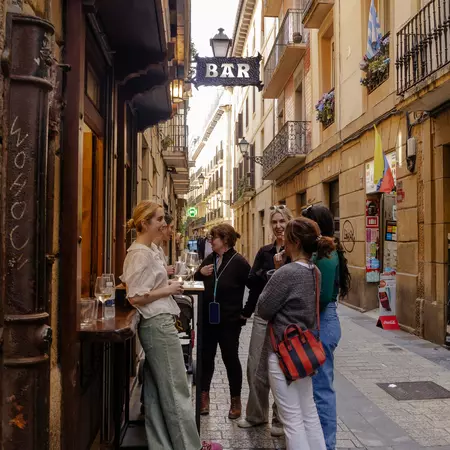 People stand outside a cafe by a small table holding glasses.