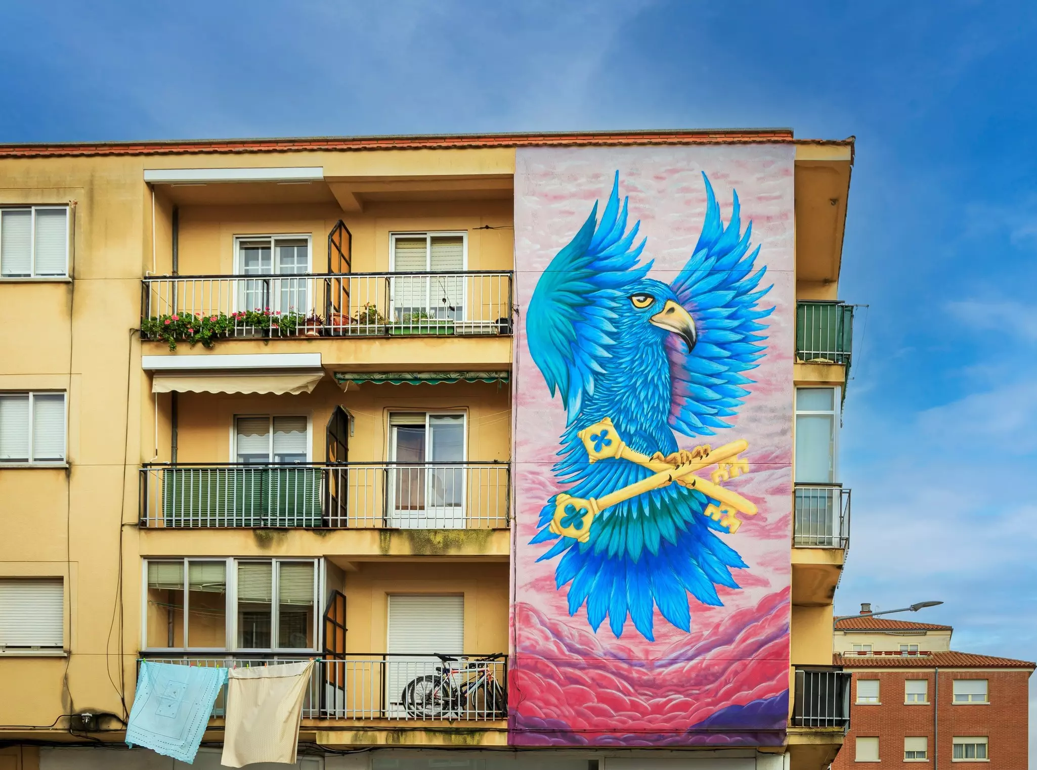 Wall art depicting a giant blue parrot carrying some keys on the side of an apartment block in Salamanca.