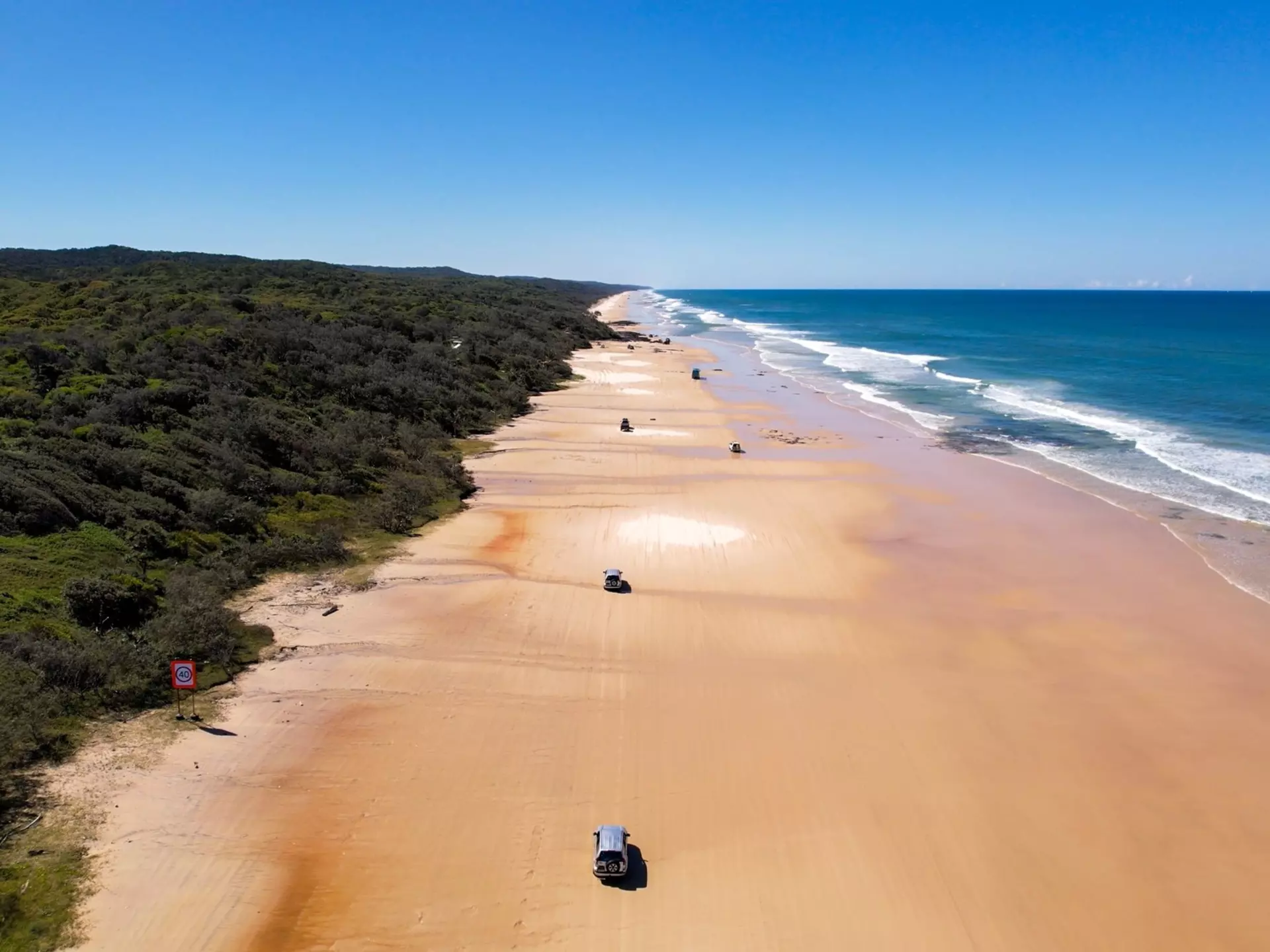 An overhead view of 4WD vehicles driving on a wide beach