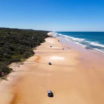 An overhead view of 4WD vehicles driving on a wide beach